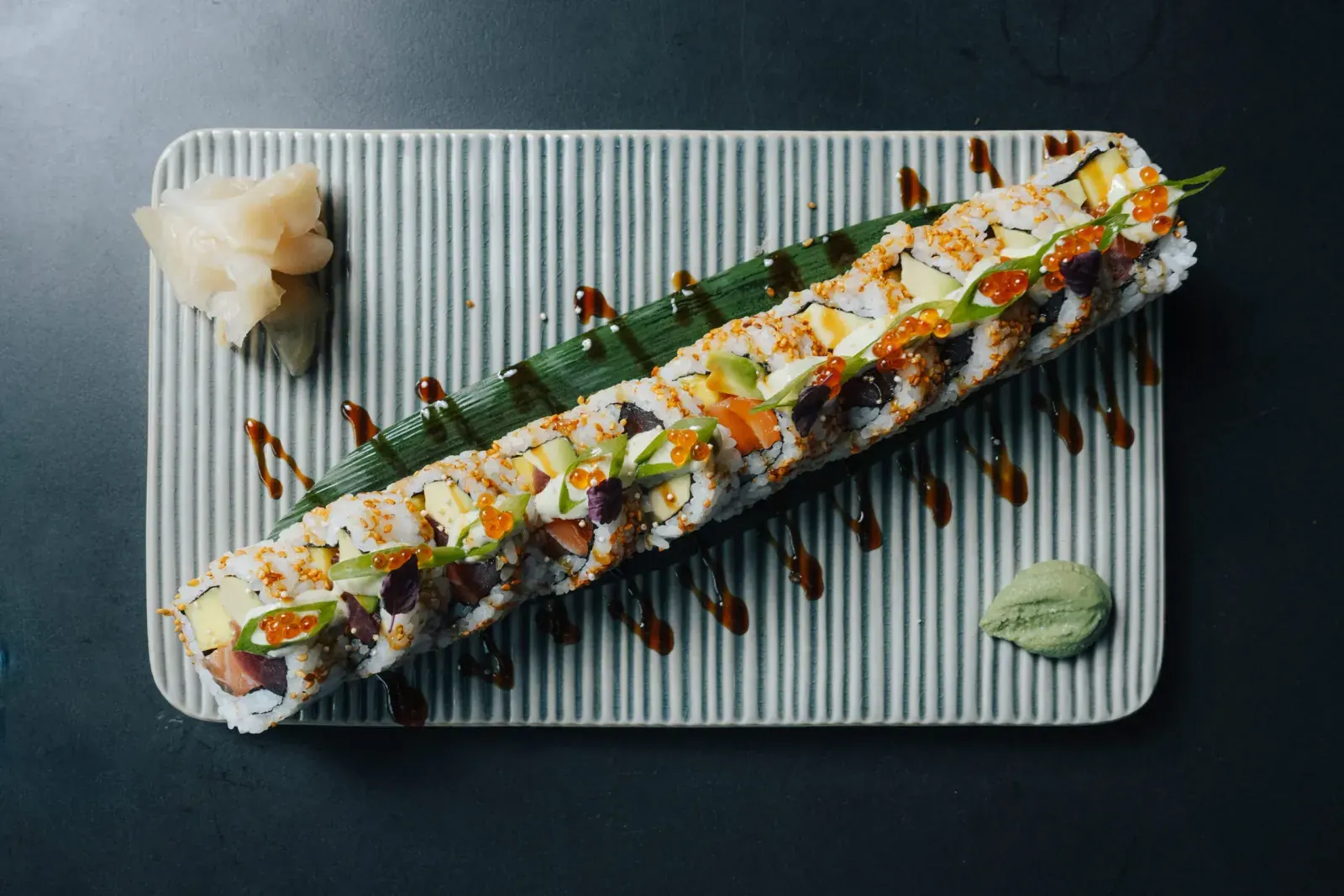 Lange Signature-Rolle mit Lachs, Thunfisch und Kaviar auf geripptem Teller, von oben fotografiert